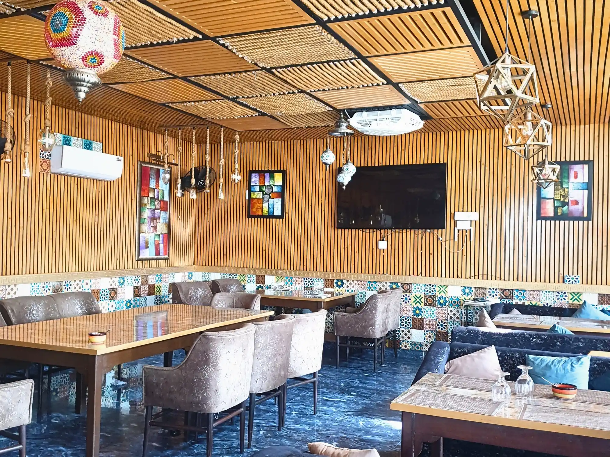 The wood-panelled dining room at Aangan, tables laid beneath a slatted ceiling