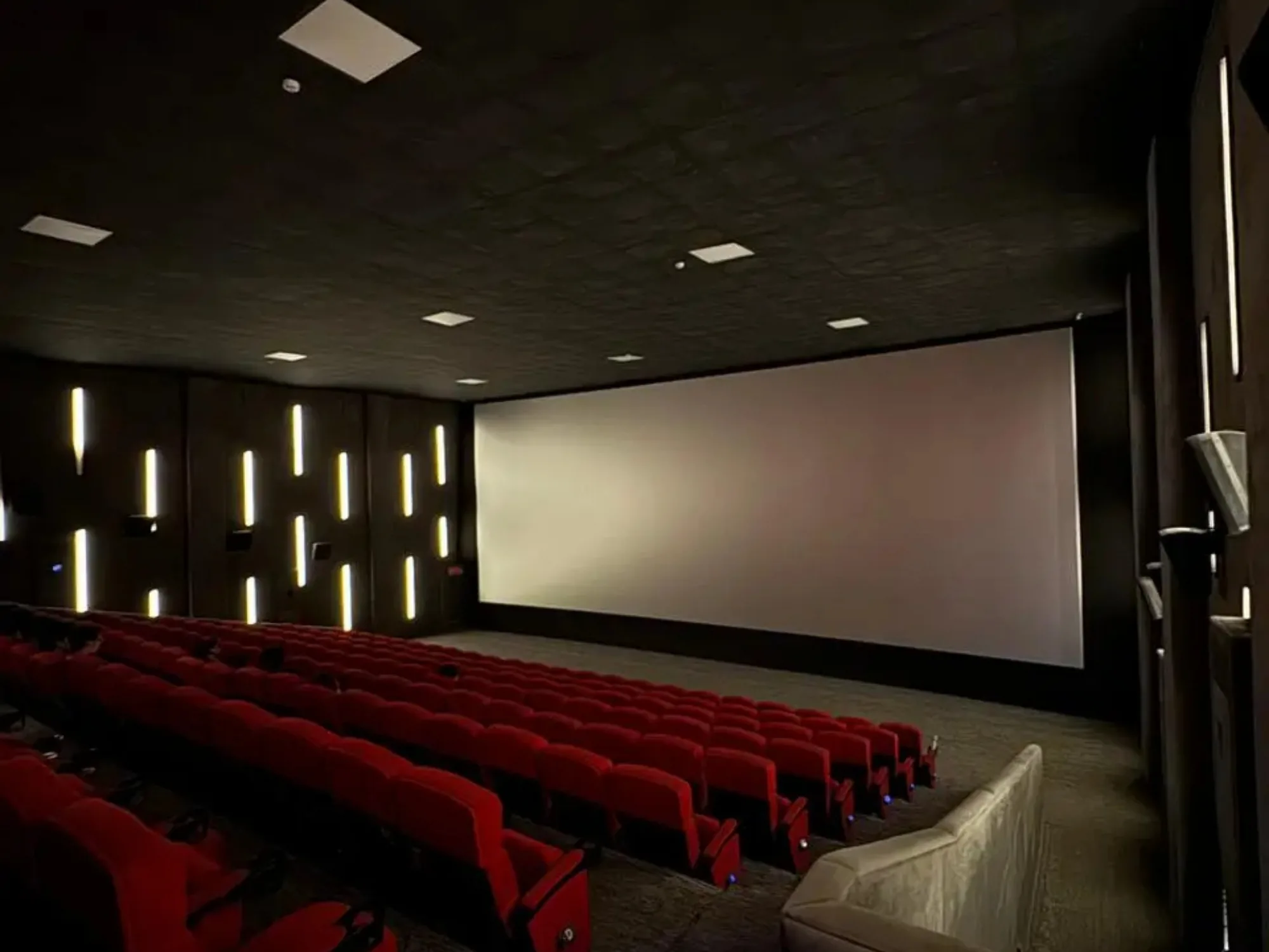 A CineStar auditorium in low light, the screen dark and the aisle lights on