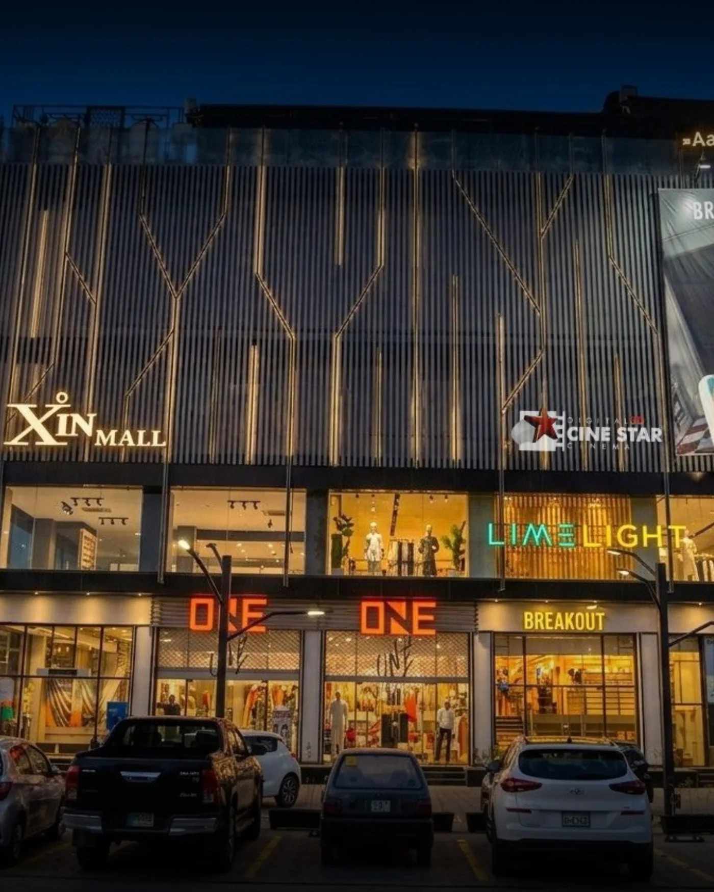 Xin Mall on Queens Road, Sargodha, lit at dusk with its tenants' signage across the frontage