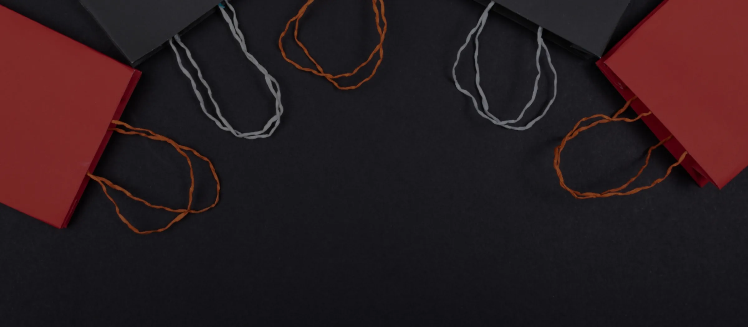 Red gift bags with twisted paper handles laid flat on a dark background